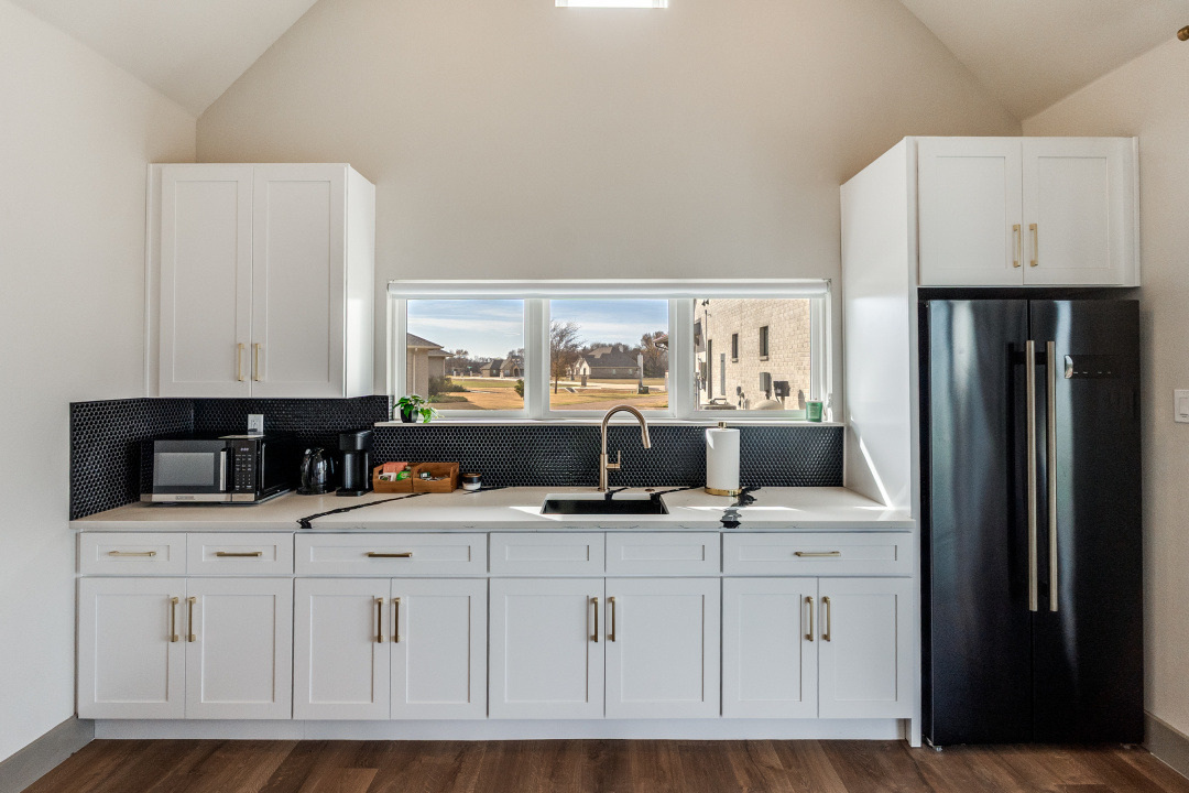 Custom ADU kitchen with white cabinetry and black backsplash by Estate ADU in Highland Park, TX.