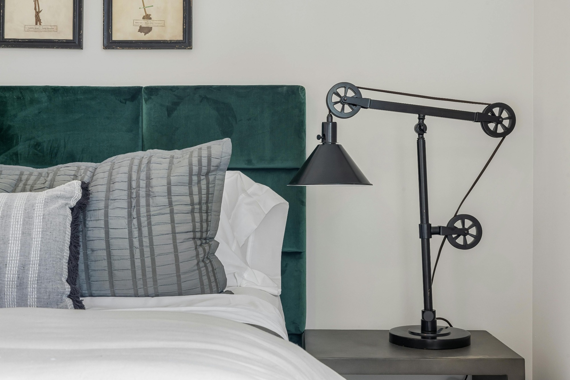Stock image of a bedroom with a green velvet headboard gray pillows and a black industrial table lamp