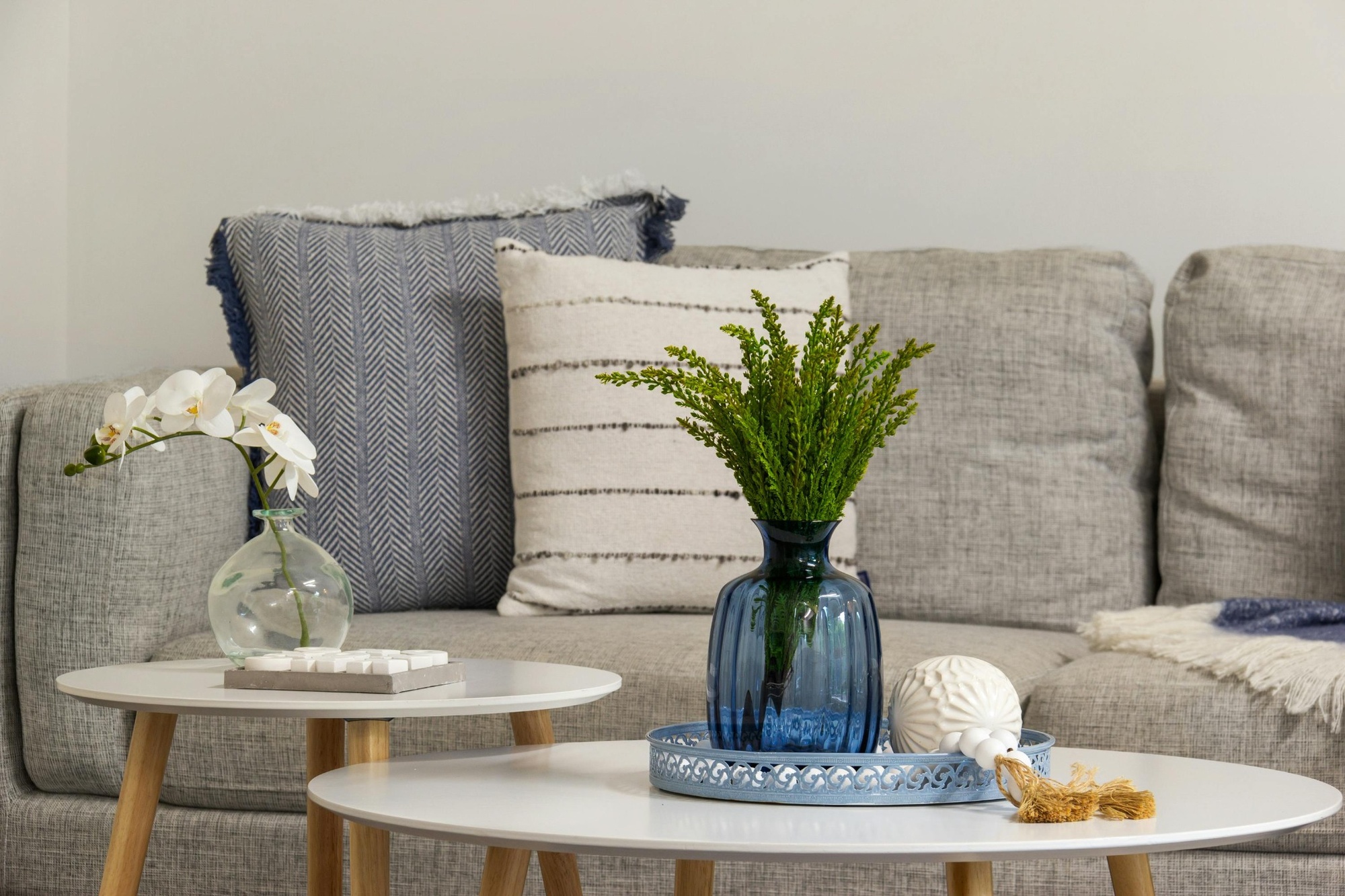 Stock image of a gray sofa with blue and striped pillows and decor on round white tables