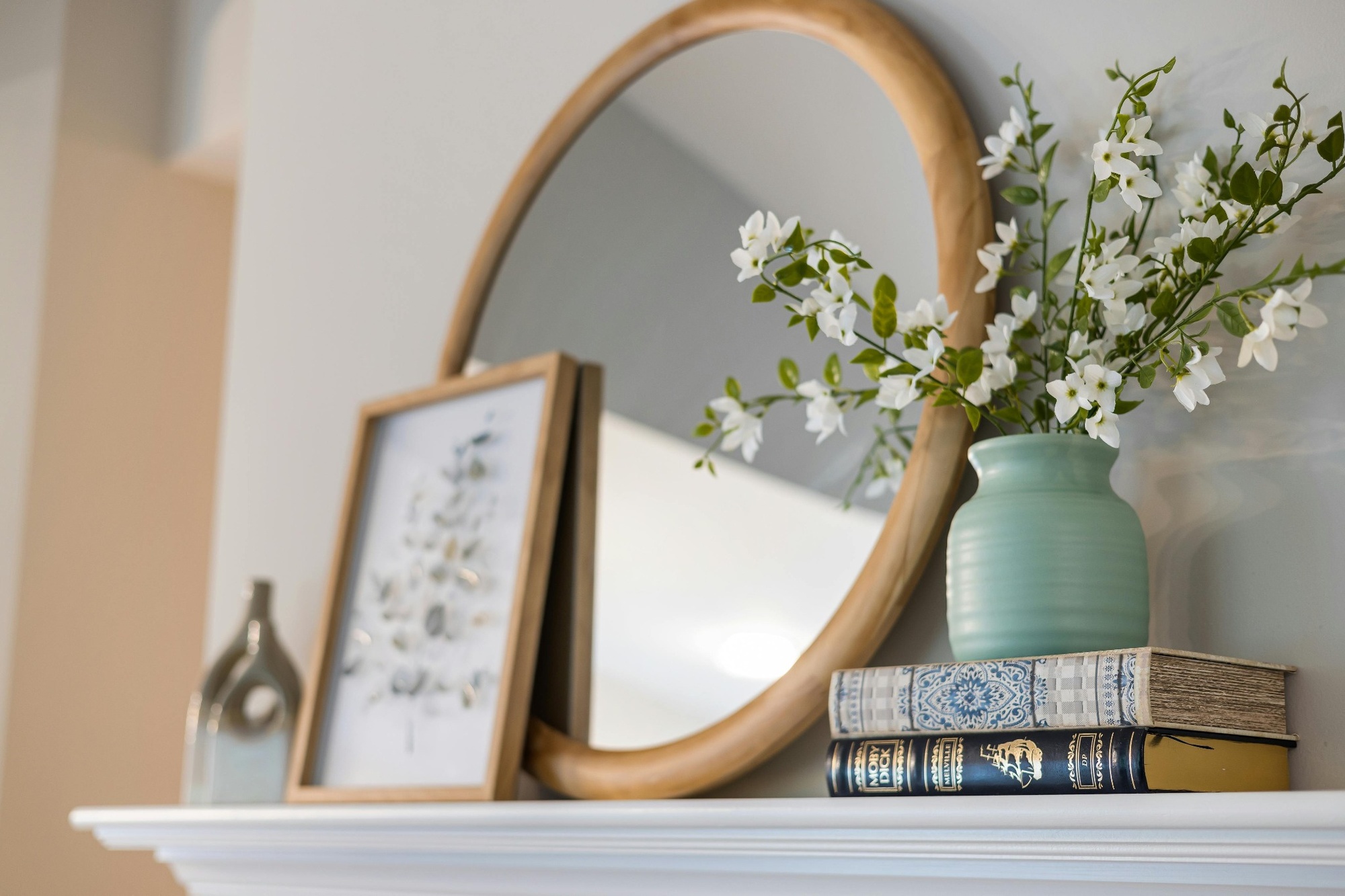 Stock image of a mantel with a round wood mirror art print green vase and stacked vintage books