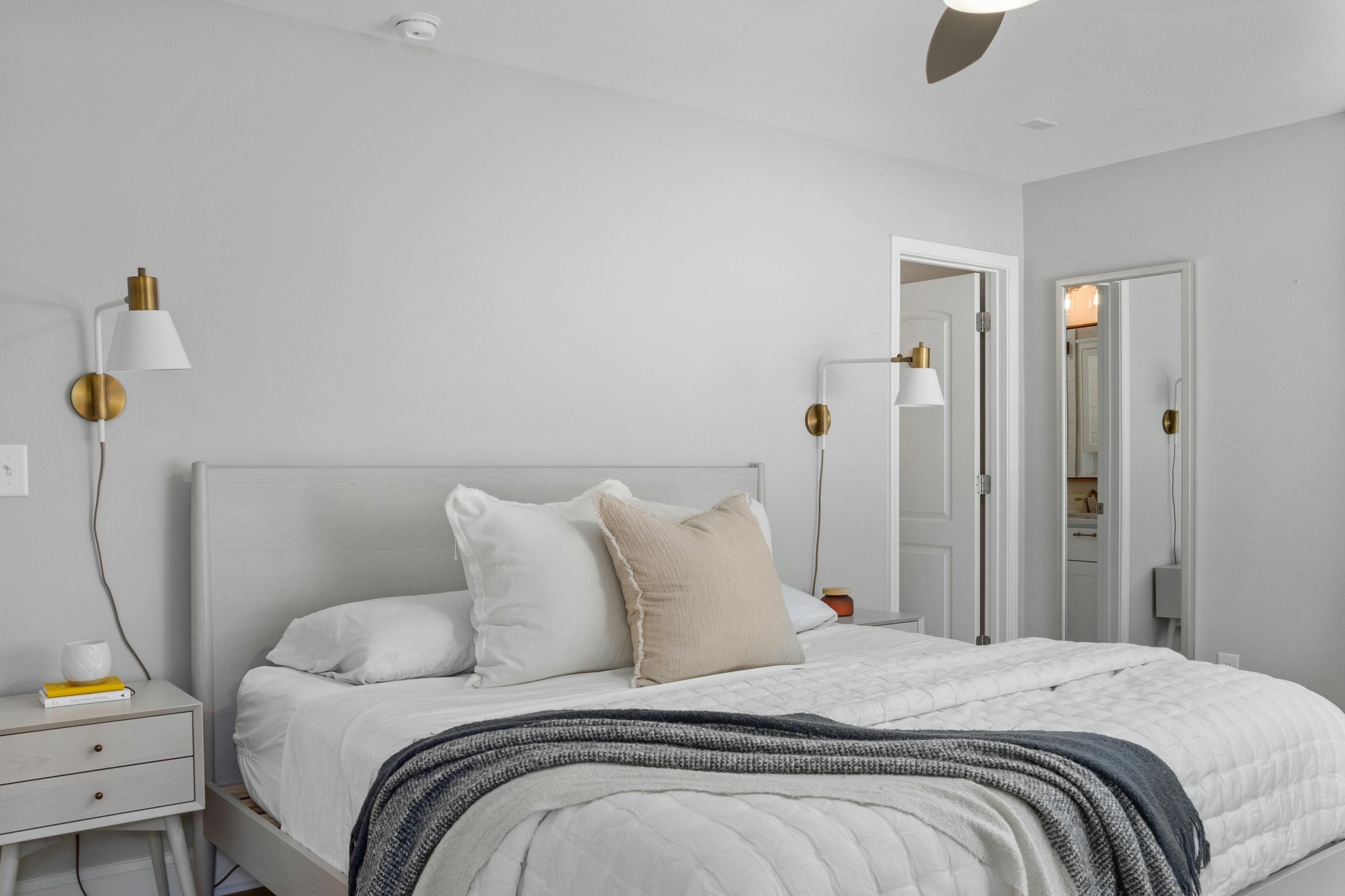 Stock image of a neutral bedroom with white bedding beige pillows and brass wall sconces