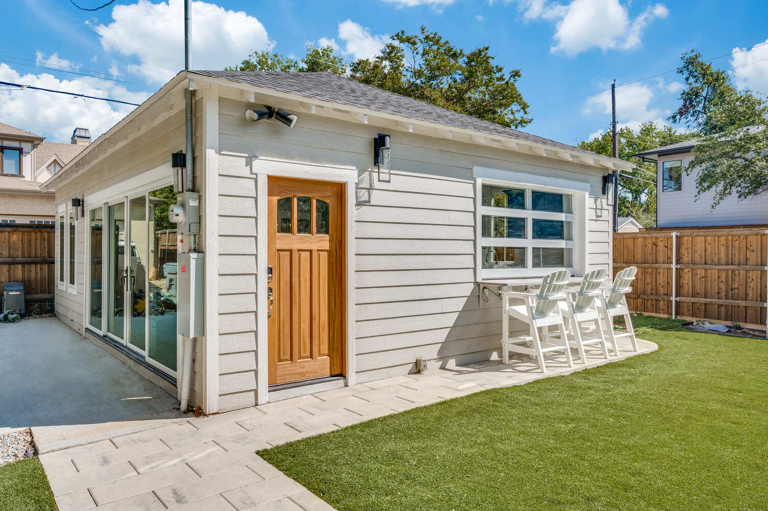 Exterior view of custom-built ADU in Dallas, TX by Estate ADU, featuring light siding, wood door, and outdoor bar seating.